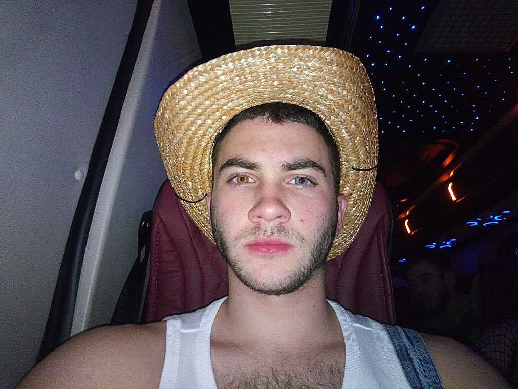 Dead-serious selfie of Sruly in a straw cowboy hat with one brown eye and one blue eye