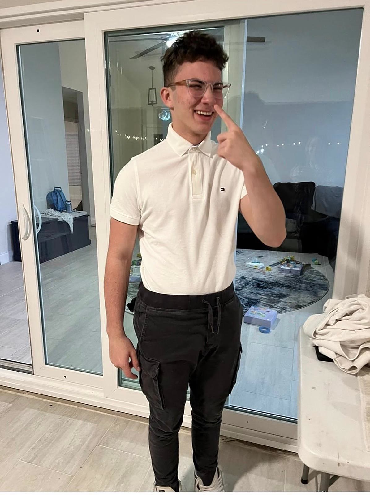 Sruly in a white polo pointing at his own nose