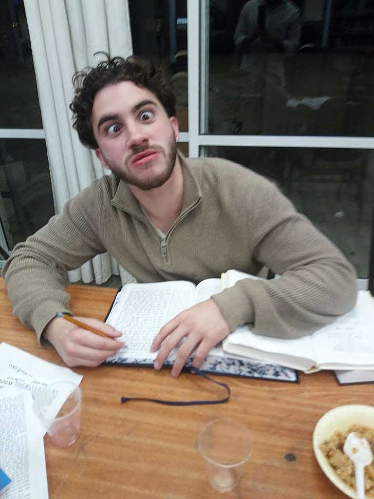 Sruly at a study table with wide bulging eyes, holding a pencil over an open book